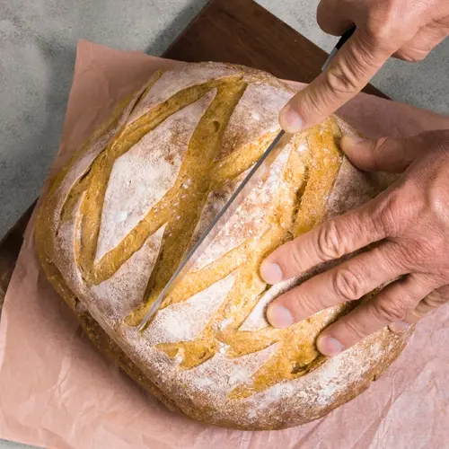 Fresh artisan sourdough loaf being sliced on a wooden cutting board — product from the online store case study