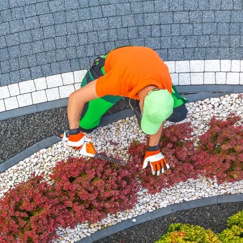 Landscaper in an orange shirt trimming shrubs along a curved paver pathway at a Utah Valley Landscaping property